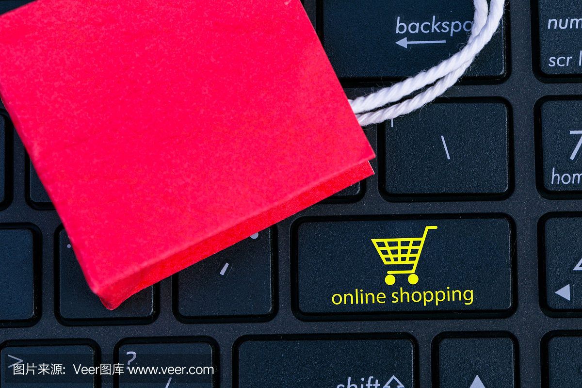 笔记本键盘上的红色纸购物袋。关于网上购物的