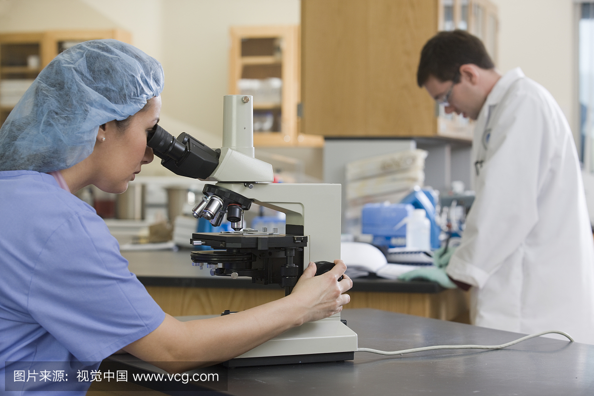 女实验室技术人员通过显微镜分析样品