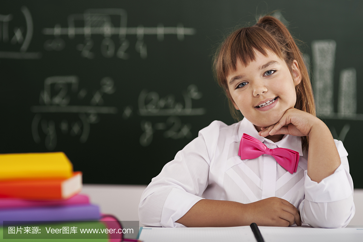 可爱的小女学生坐在教室里和她的书