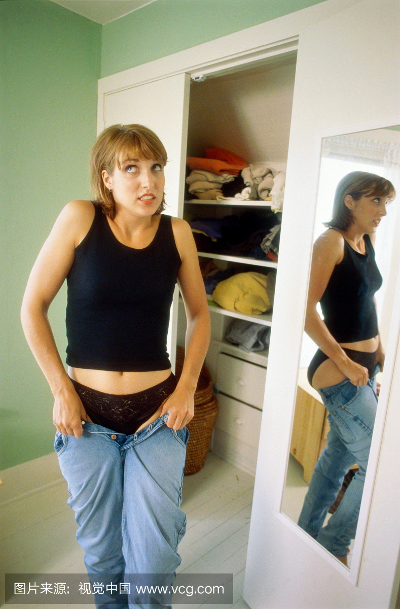 女人站在卧室里,试图穿上牛仔裤
