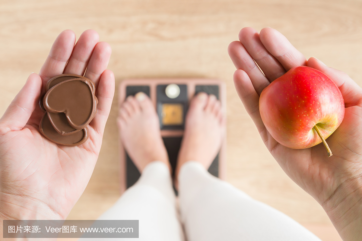 女人站在体重秤上,拿着苹果和巧克力的心。新