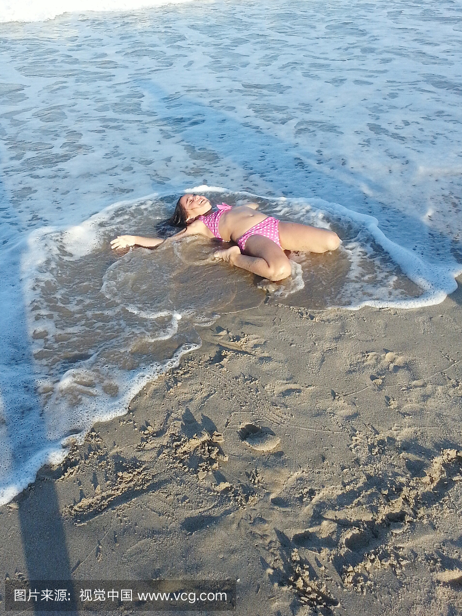 比基尼泳装中的快乐女孩躺在岸边