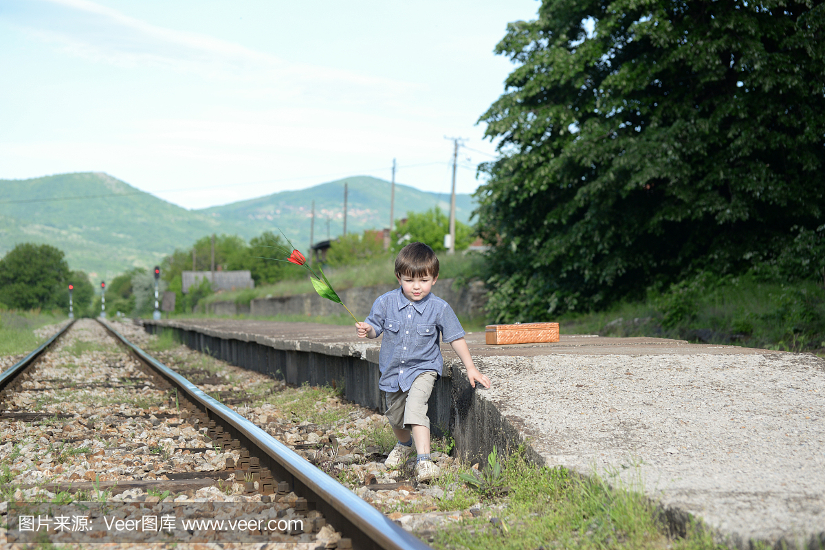可爱的小男孩走在铁路上,拿着花