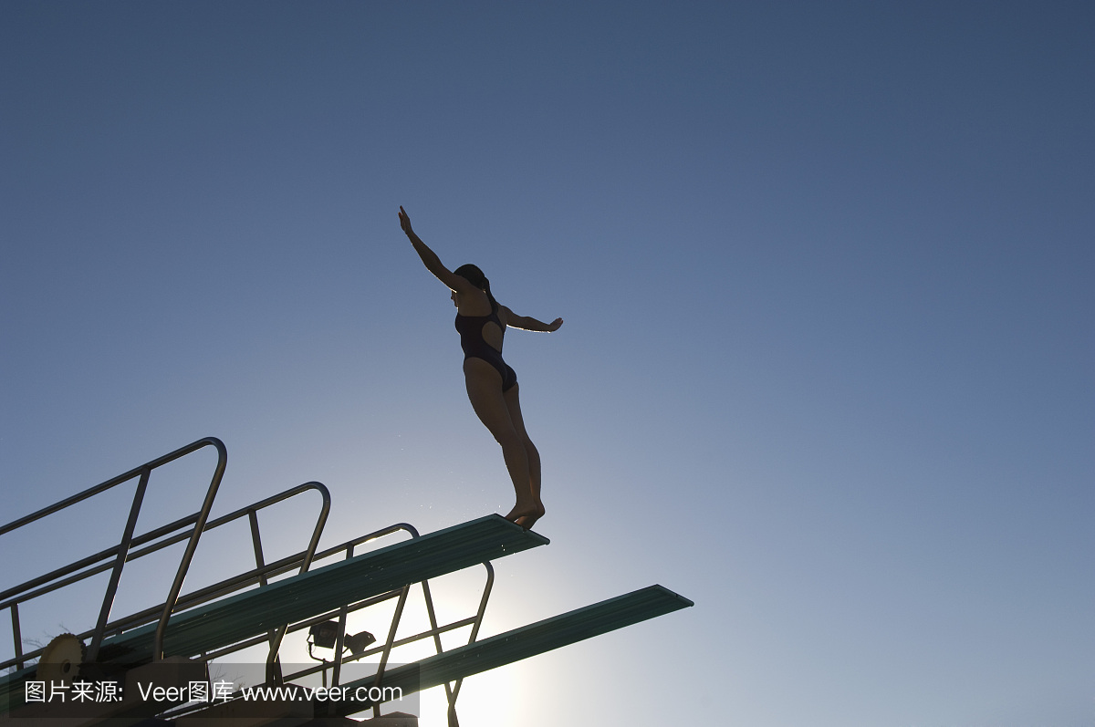 在日落时站在跳水板上的女游泳运动员