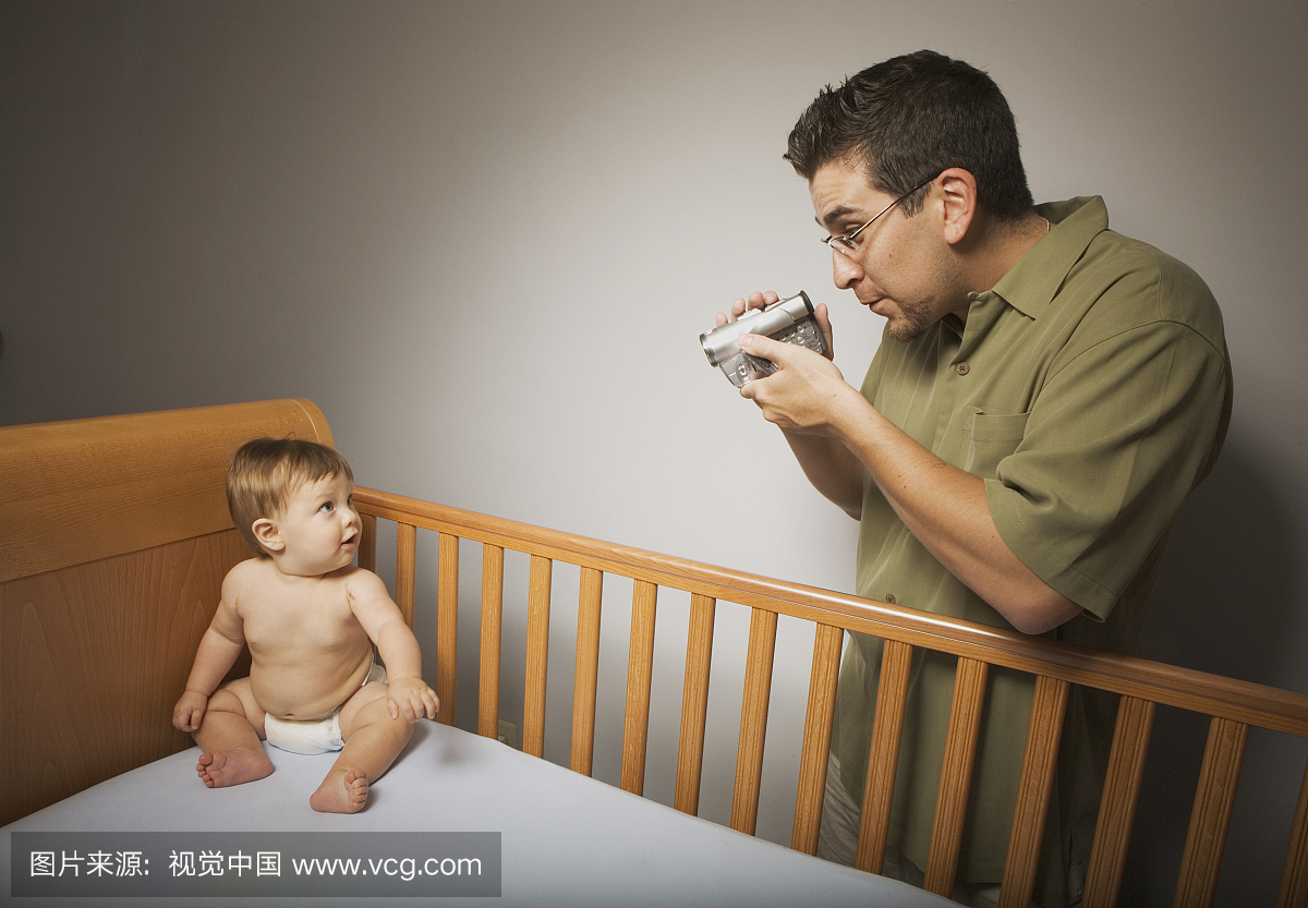 父亲拍摄的男婴(9-12个月)坐在婴儿床上