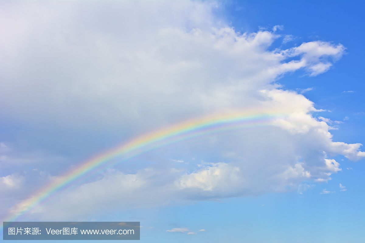 天蓝色的天空上的白色云彩下的彩虹。