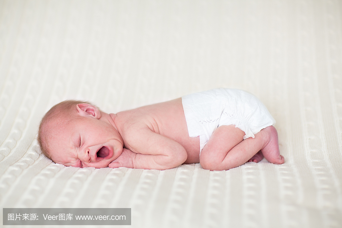 微小的打呵欠的新生婴儿在尿布上睡在针织毯子