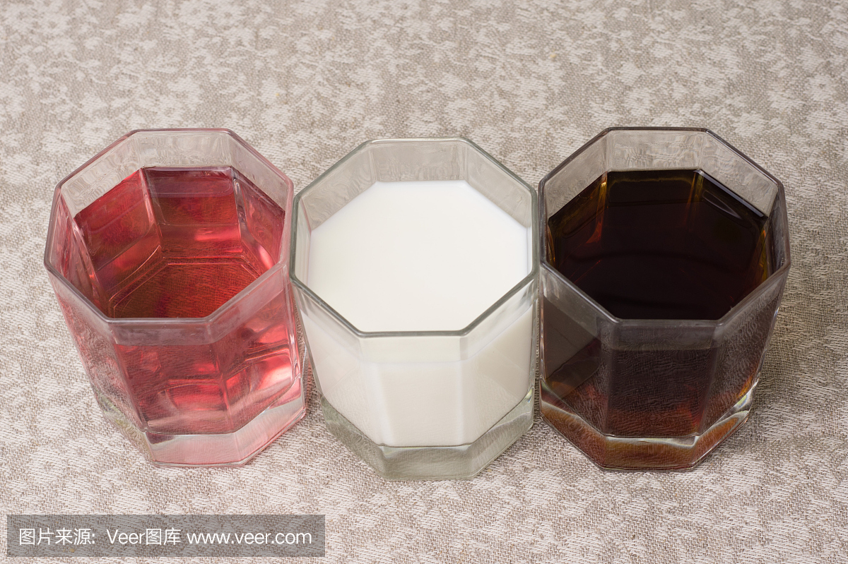 三种眼镜中各种各样的饮料在亚麻布桌布的背景